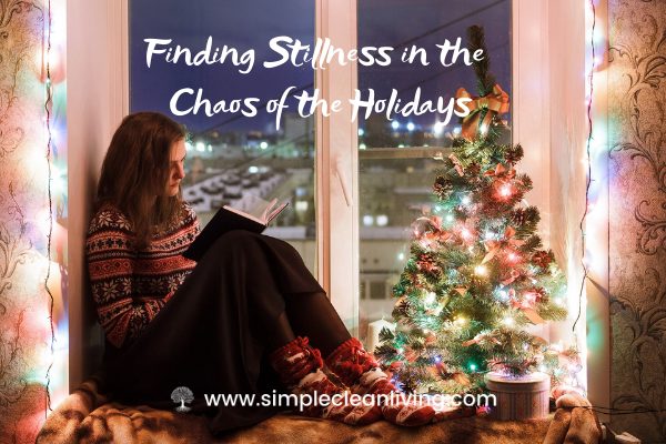 Finding Stillness in the Chaos of the Holidays- Picture of a woman sitting on a window seat reading a book next to a small lit Christmas tree