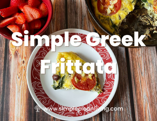 Simple Greek Frittata Recipe post- Picture of a piece of Greek frittata on a red and white plate. It is sitting on a table with the remaining pan of frittata and a red bowl filled with sliced strawberries