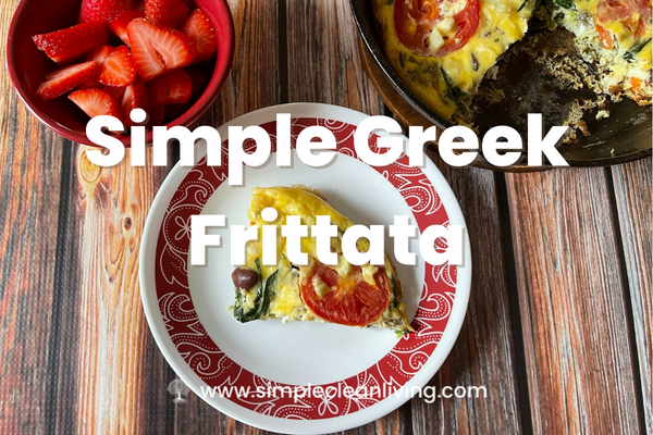 Simple Greek Frittata Recipe post- Picture of a piece of Greek frittata on a red and white plate. It is sitting on a table with the remaining pan of frittata and a red bowl filled with sliced strawberries