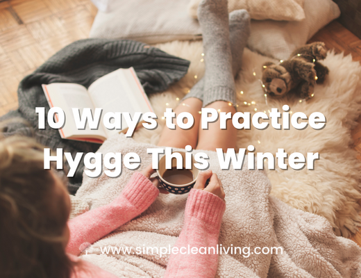 10 Ways to Practice Hygge This Winter- Picture of a person holding a cup of cocoa snuggled up with a book wearing warm socks