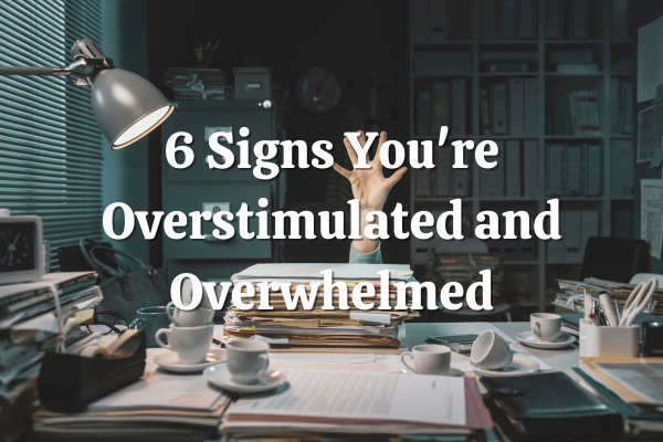 6 Signs Your Overstimulated and Overwhelmed Blog post title with picture of a hand reaching up behind a desk covered with a lot of paperwork