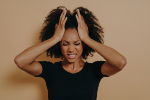 Picture of stressed woman wearing a black shirt holding her hands on the sides of her head with a distressed look on her face