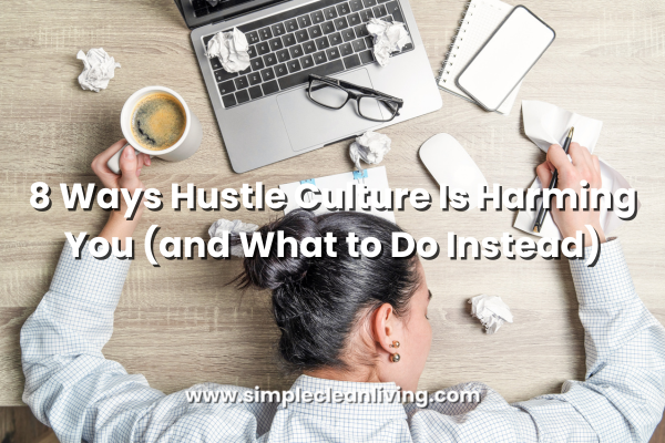8 Ways Hustle Culture is Harming You blog post title over picture of a woman wearing a white business shirt. She is slumped over on her desk in exhaustion and is surrounded by her laptop, phone and many crumpled pieces of paper.